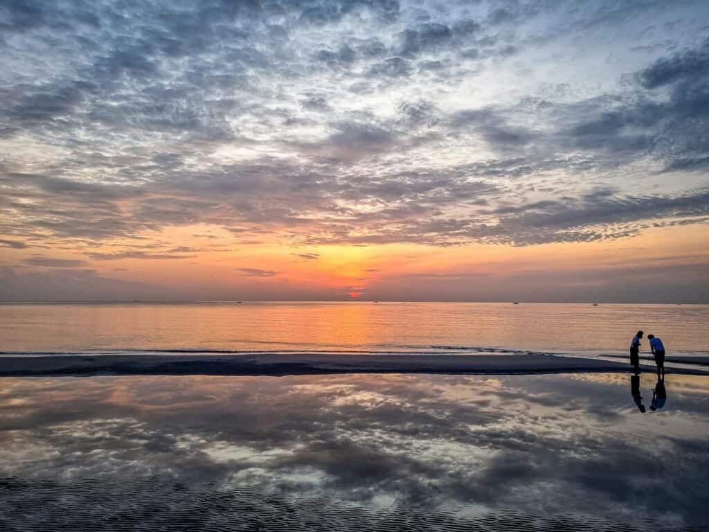 Peaceful sunrise over Hua Hin Beach with reflections in the calm water, capturing serene beauty.