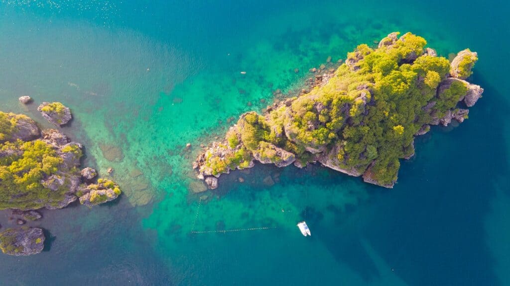Stunning aerial shot of a rocky island with lush greenery in Krabi, Thailand, surrounded by clear turquoise water.